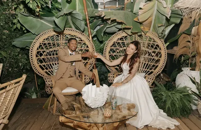 Bride and groom sitting in wicker peacock chairs, surrounded by lush tropical foliage