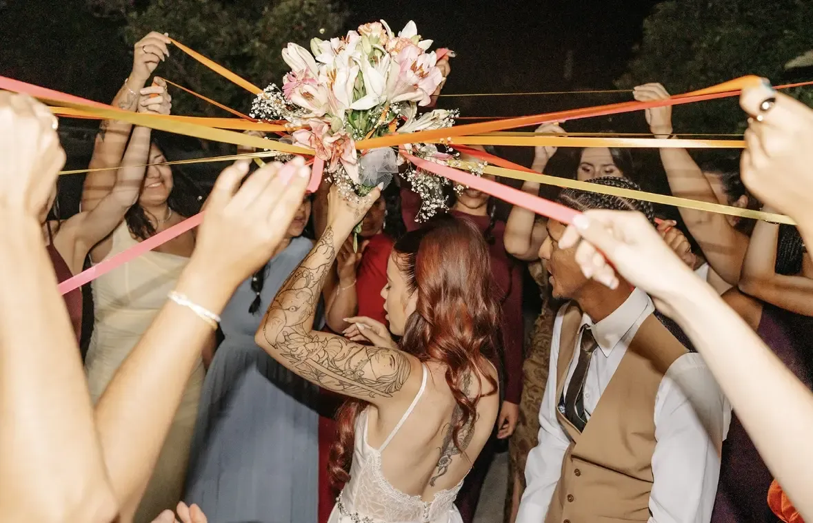 Bride tossing bouquet with colorful ribbons held by guests