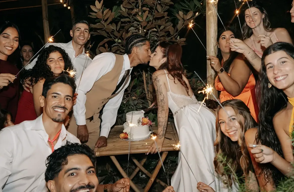 Newlyweds kissing over wedding cake surrounded by guests with sparklers
