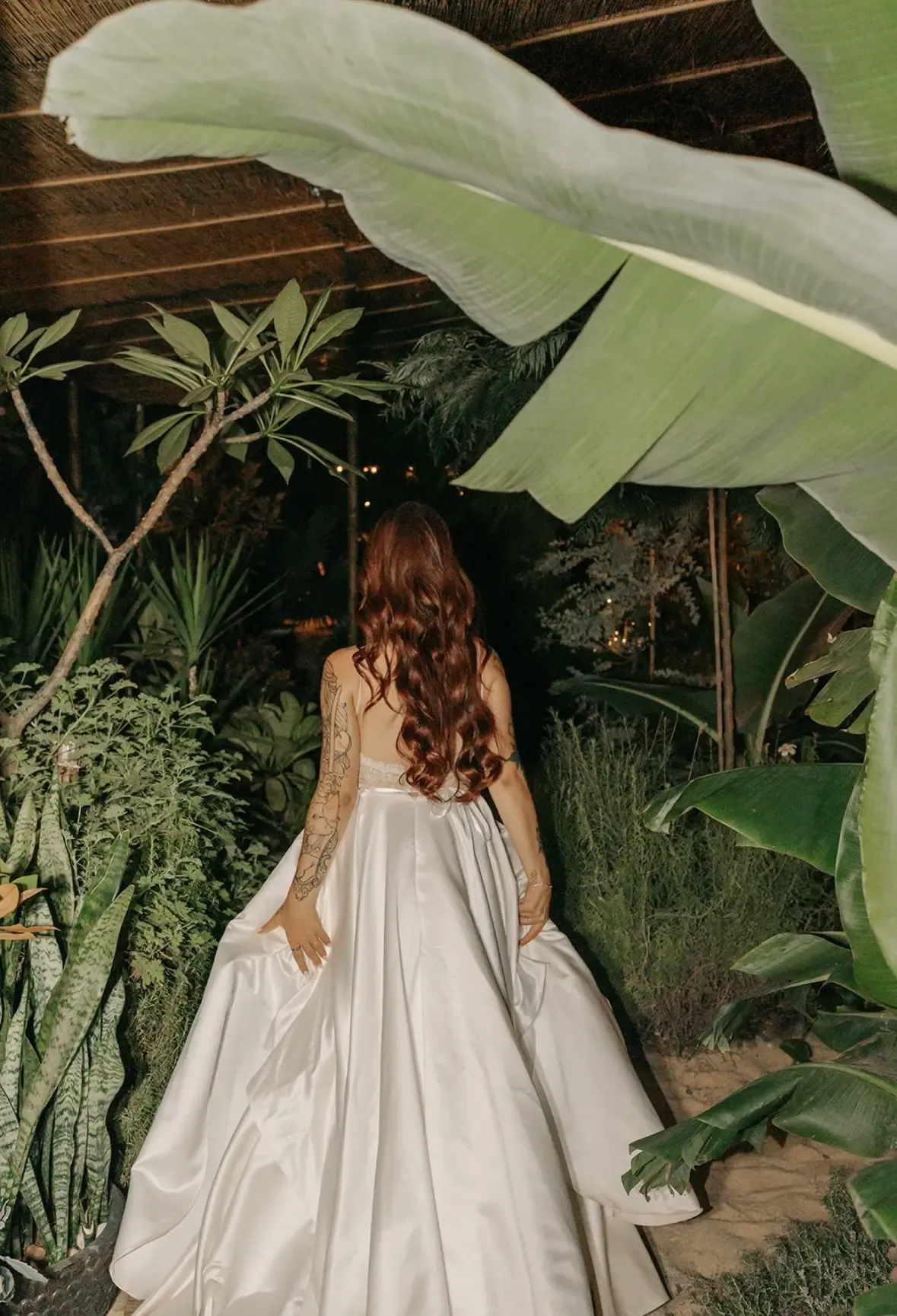 Bride seen from behind walking through tropical corridor with banana leaves