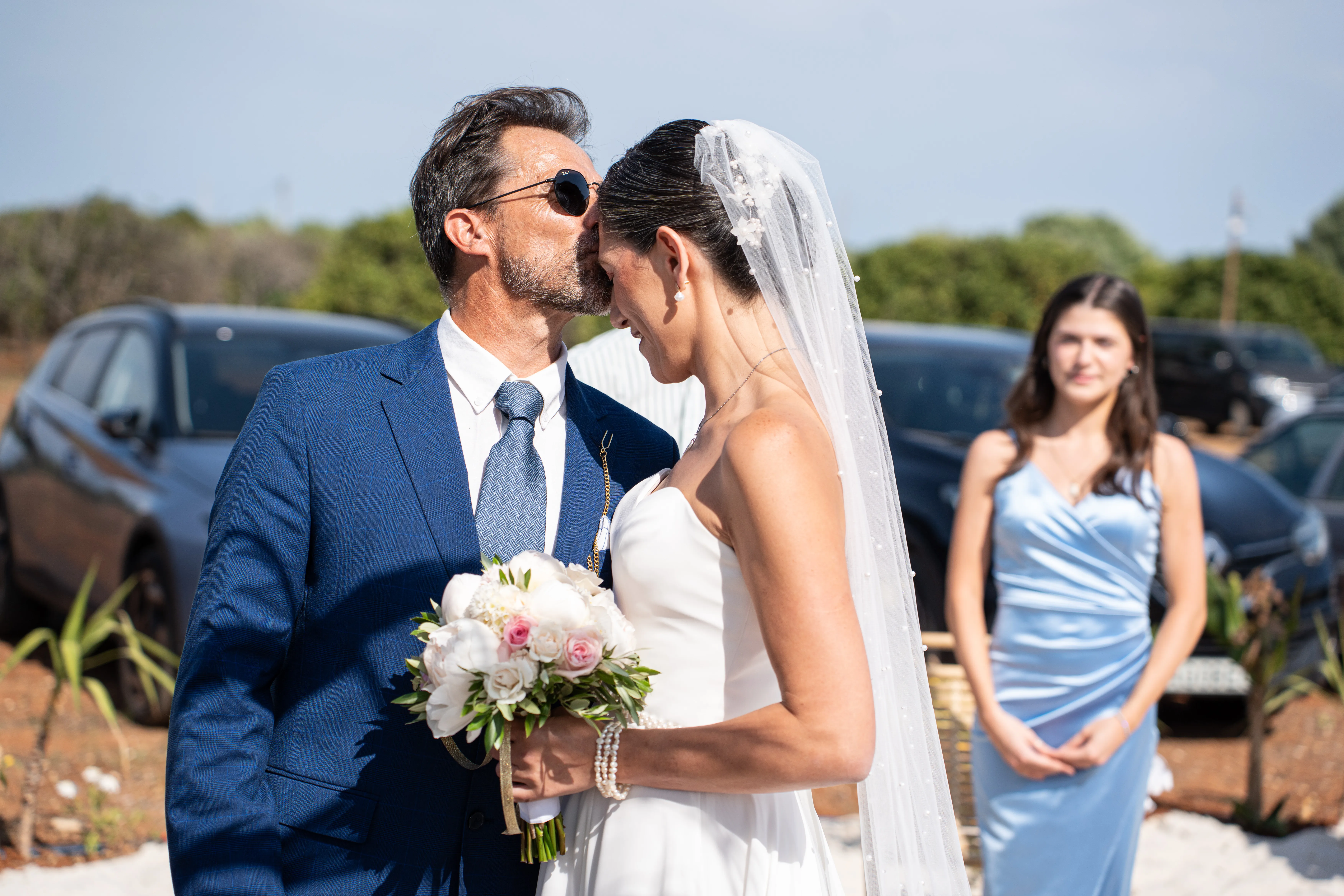Bride and groom kissing with peony bouquet, bridesmaid in the background