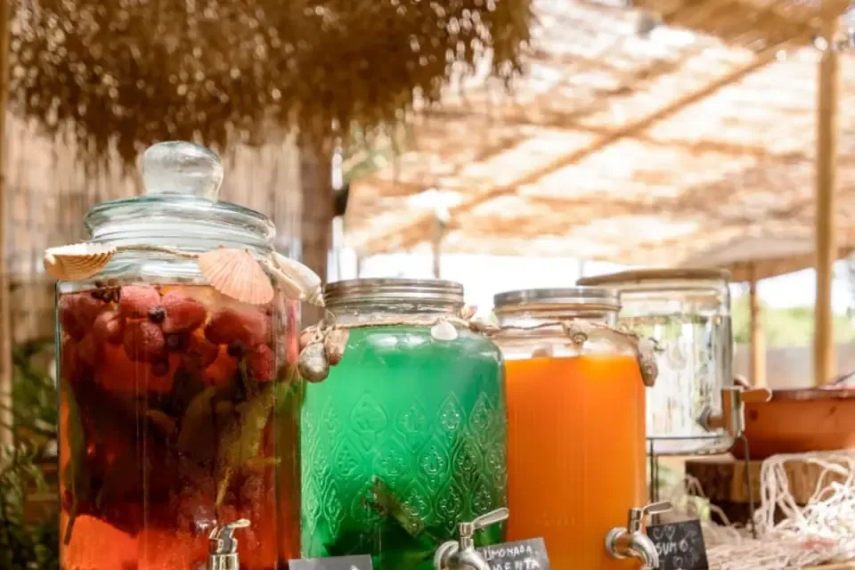 Three glass jars with red fruit sangria, mint lemonade and orange juice, under a thatched canopy