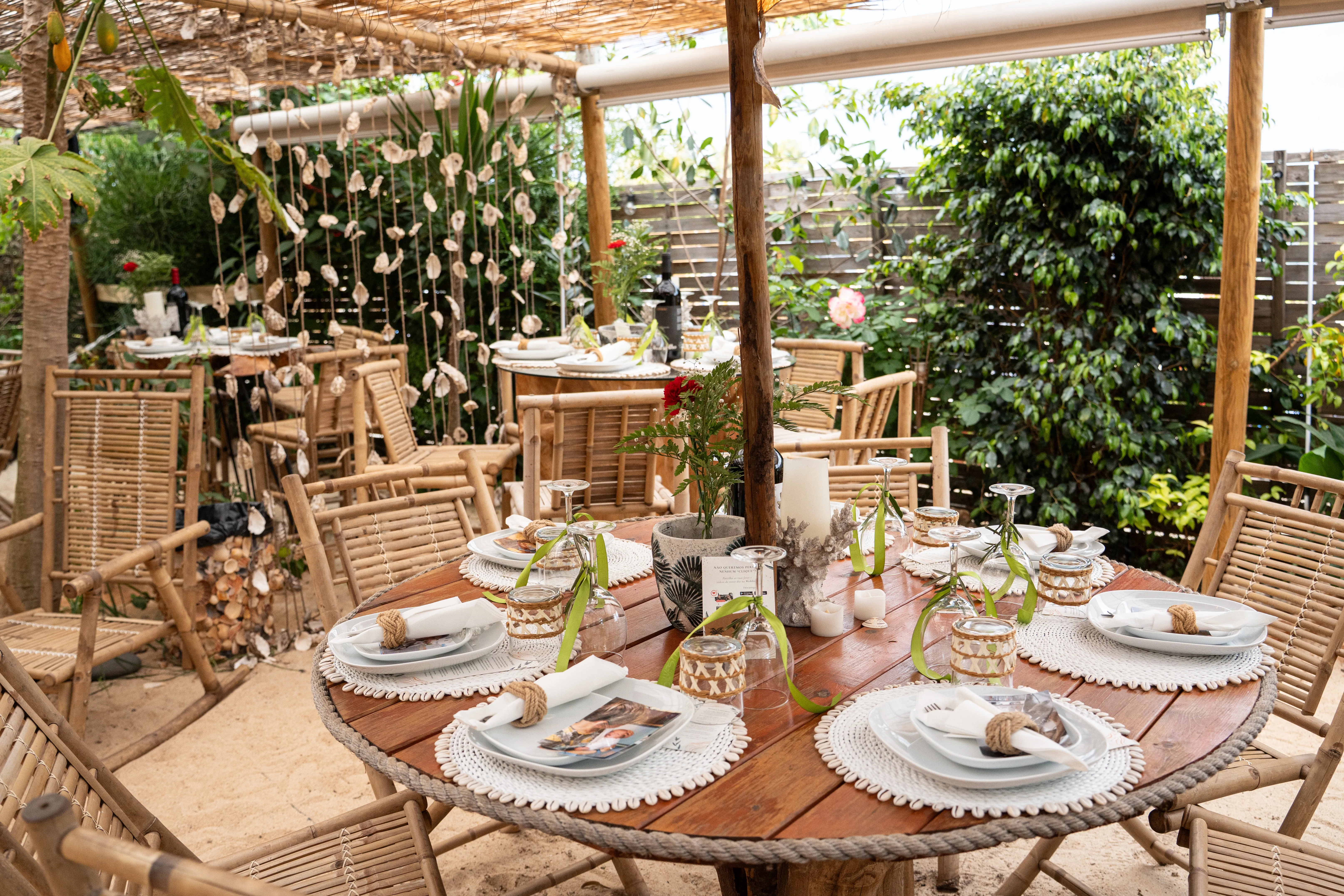 Round bamboo table with seashell garland, glasses, plates and cutlery set for an event